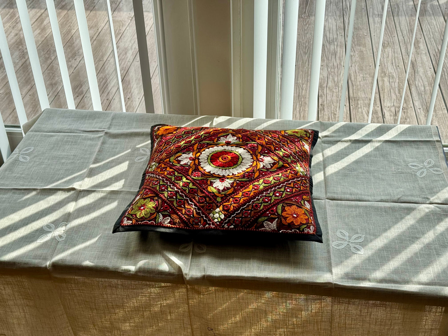 Cushion cover featuring vibrant Kutchi embroidery with intricate mirror work and colorful thread patterns on a textured fabric.