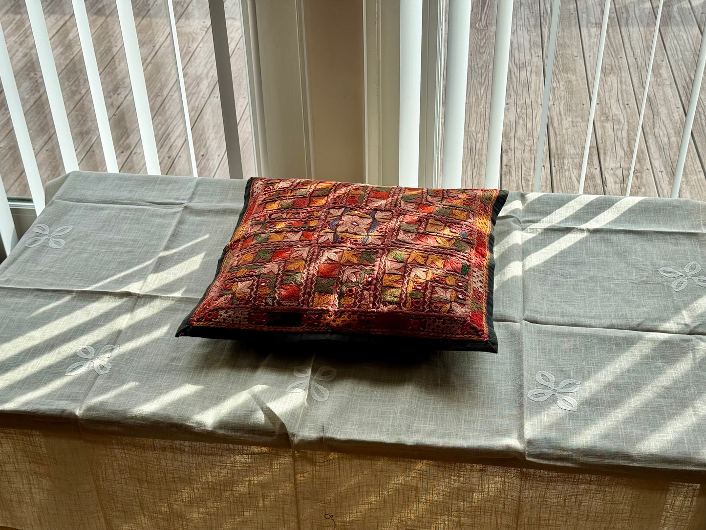 Cushion cover featuring vibrant Kutchi embroidery with intricate mirror work and colorful thread patterns on a textured fabric.