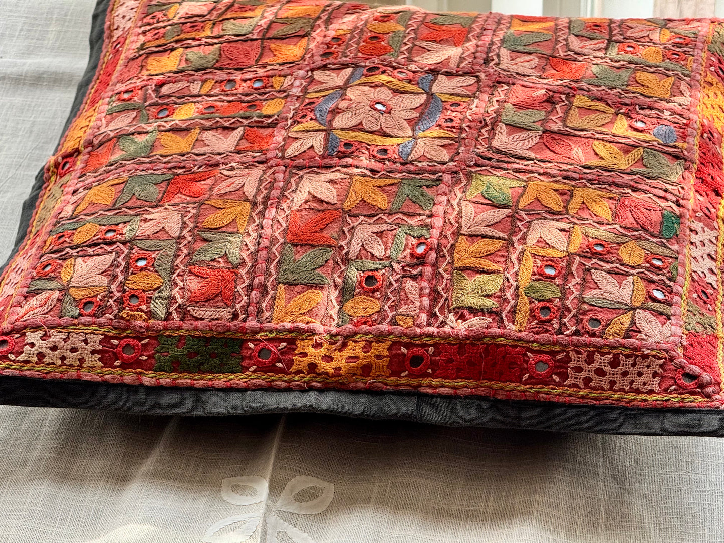 Cushion cover featuring vibrant Kutchi embroidery with intricate mirror work and colorful thread patterns on a textured fabric.