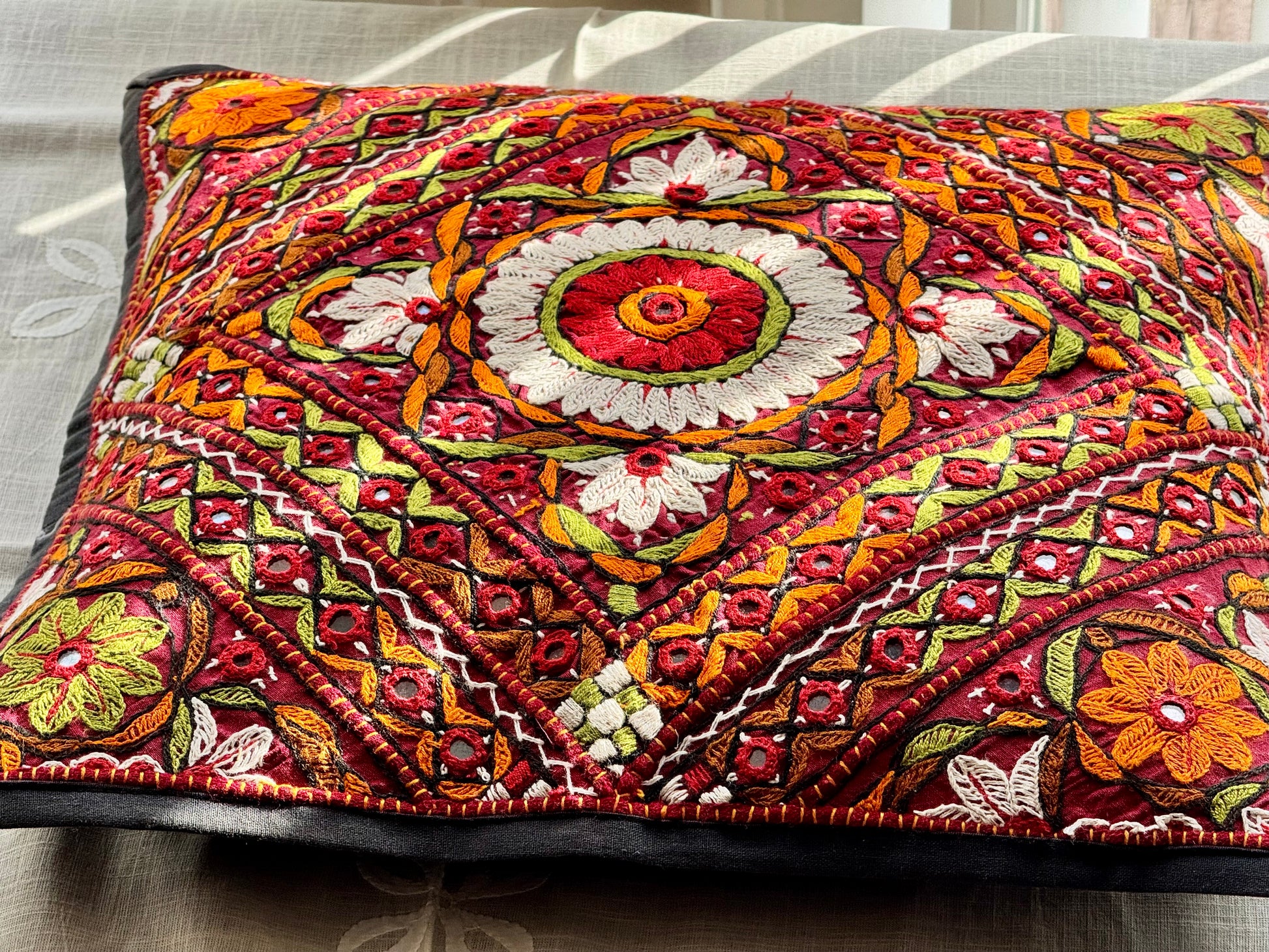Cushion cover featuring vibrant Kutchi embroidery with intricate mirror work and colorful thread patterns on a textured fabric.