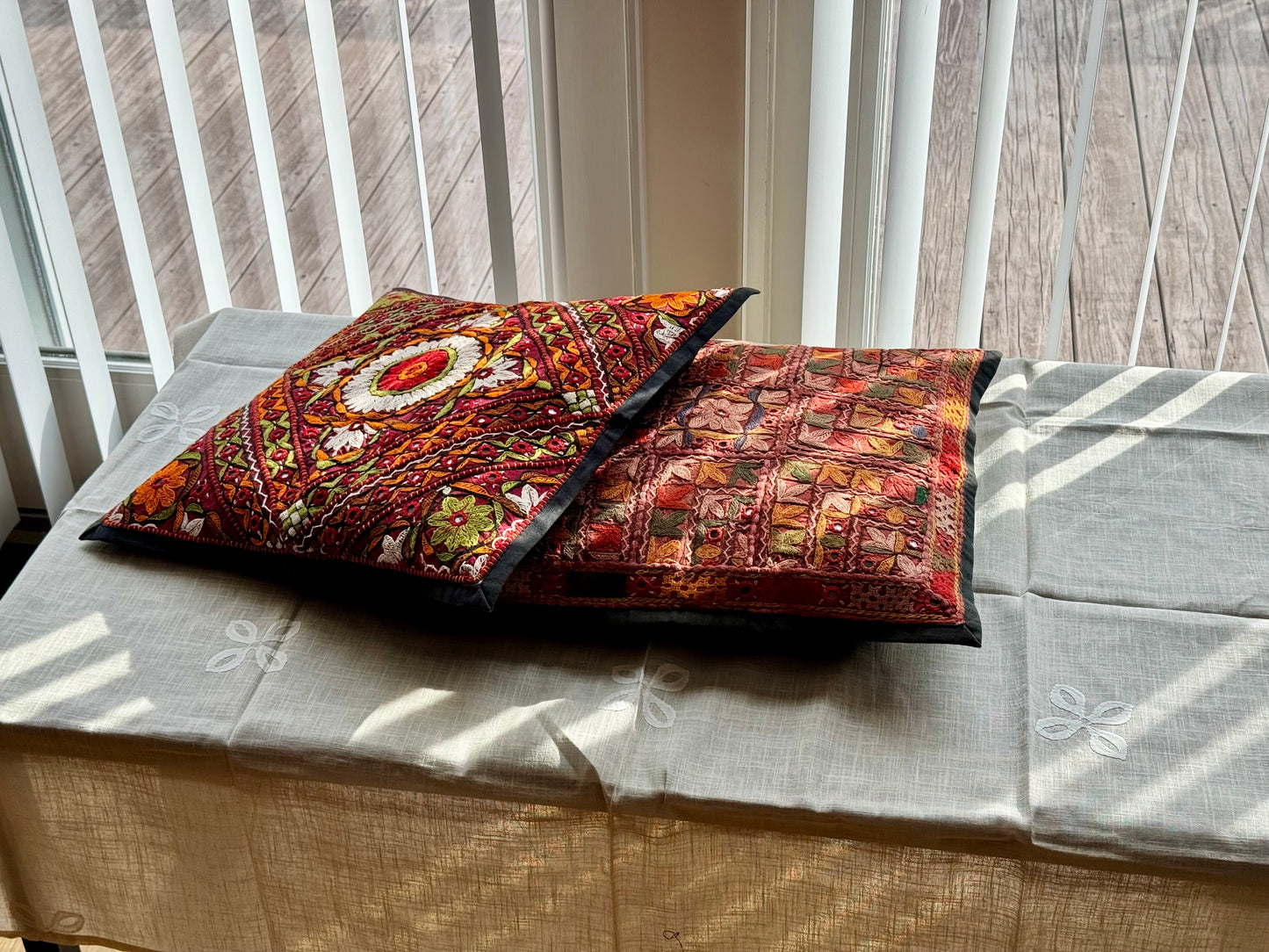 Cushion cover featuring vibrant Kutchi embroidery with intricate mirror work and colorful thread patterns on a textured fabric.