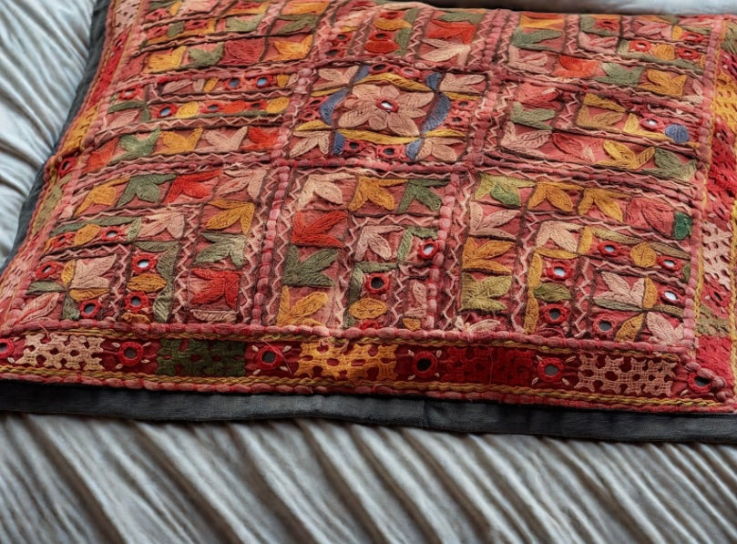 Cushion cover featuring vibrant Kutchi embroidery with intricate mirror work and colorful thread patterns on a textured fabric.